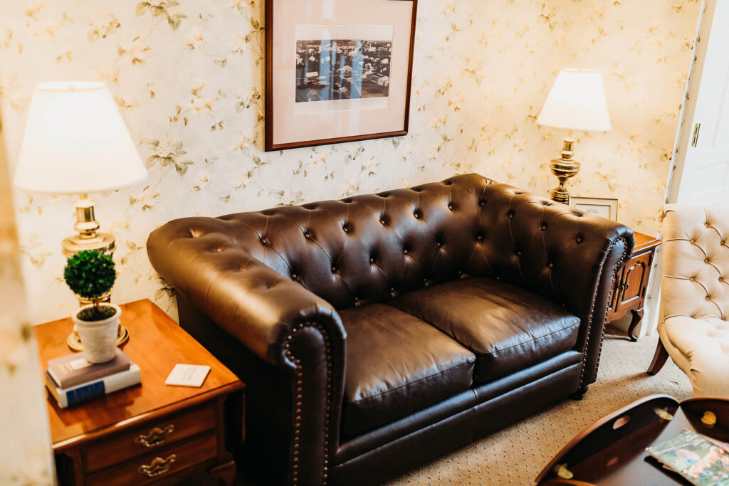 A large leather couch sitting next to two antique side tables with lamps on the top.