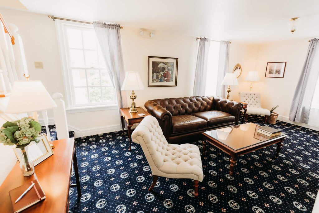 Sitting room featuring two comfortable chairs, a brown leather couch, and stairs to the left of them leading to a guest room.